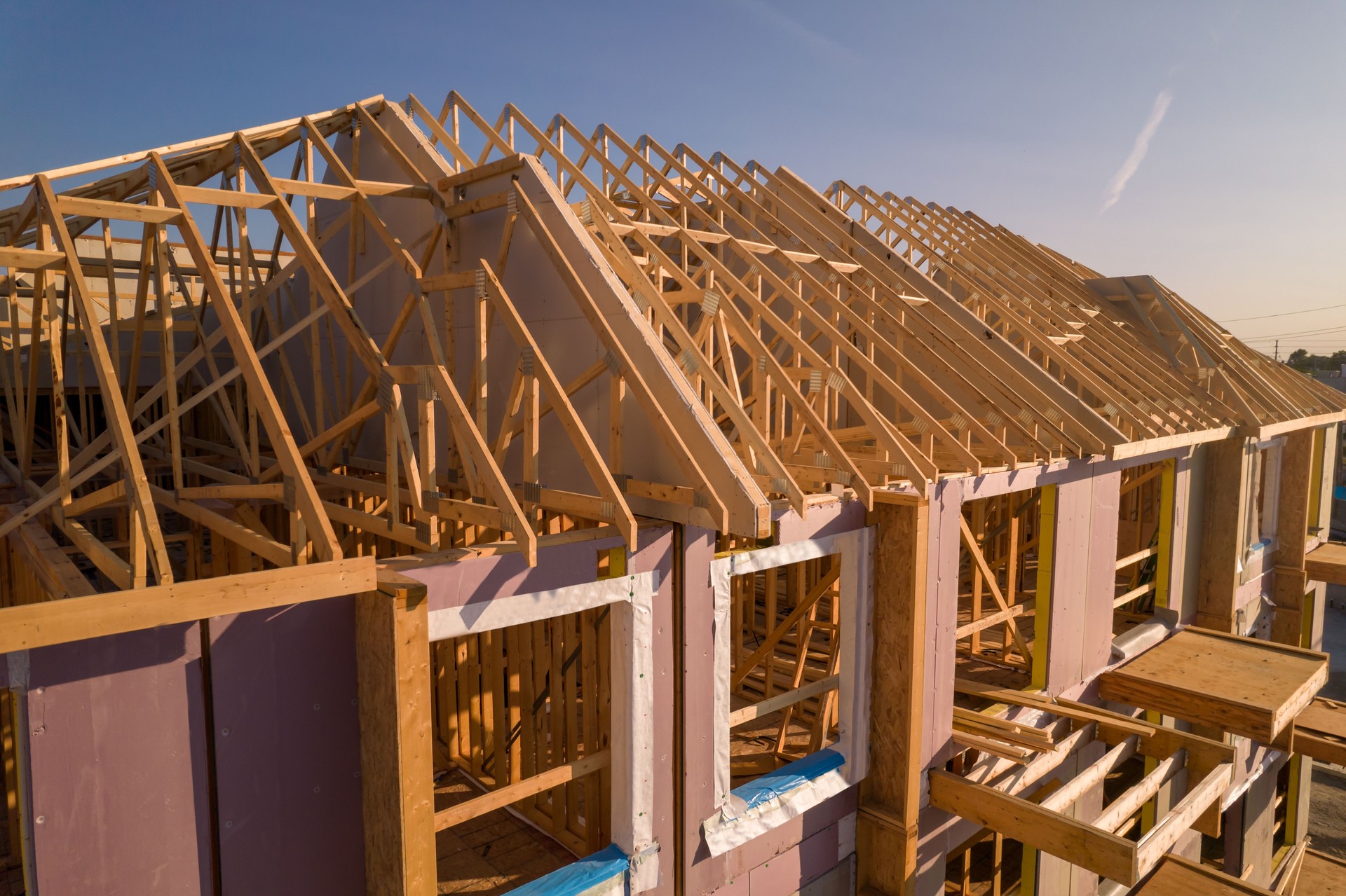 Roofing construction aerial. Wooden roof frame installation of the house. Truss beams structures on new home view from above. Golden hour. House or family home construction and real estate.